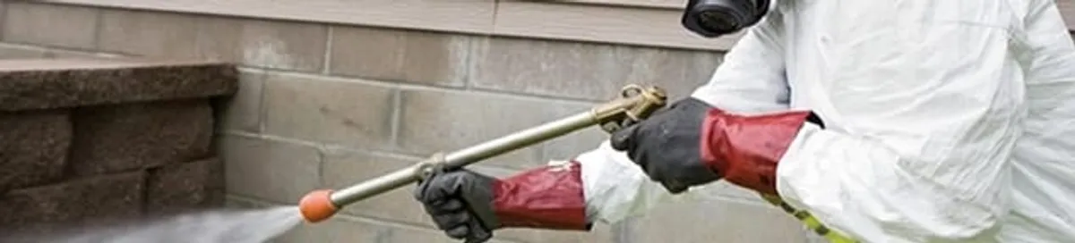 Pest control technician applying exterior insect treatment along a home foundation in Tallahassee, FL