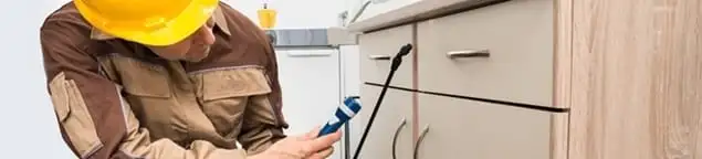 Roach exterminator applying treatment under kitchen cabinets in Tallahassee, FL