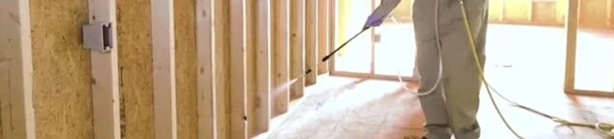 Termite treatment technician applying spray along framing and unfinished walls in Tallahassee, FL