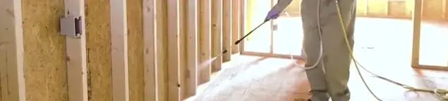 Termite treatment technician applying spray along framing and unfinished walls in Tallahassee, FL